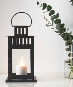 Black Lantern with lit candle next to vase with foliage