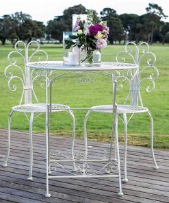 White metal table with two chairs set with floral arrangement out doors