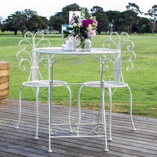 White metal table with two chairs set with floral arrangement out doors