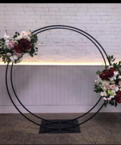 Circular black metal arch with floral arrangements attached in front of textured wall