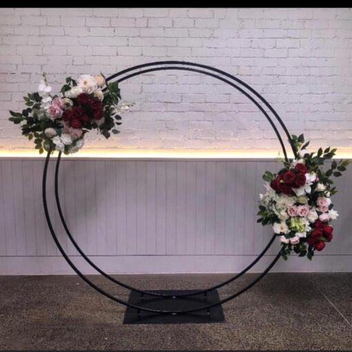 Circular black metal arch with floral arrangements attached in front of textured wall