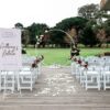 White round arch, 32 white chairs, welcome sign and easel, aisle runner with a green leafy backdrop