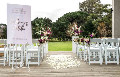 Modern outside wedding setting showing chairs, plinths with floral arrangements and signage