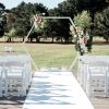 White Hexagon Arch with florals, white wedding chairs with a green leafy backdrop