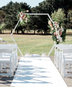 White Hexagon Arch with florals, white wedding chairs with a green leafy backdrop