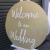 Gold wedding signage in circular gold sign with white scrip writing that says "Welcome to our wedding"