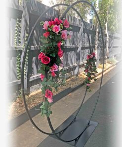 Metal double circular arch with pink flowers standing in driveway