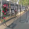Black metal double circle arch with flowers and a metal welcome stand in front of grey wooden fence