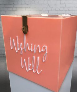 Side angle of 300mm square blush pink acrylic wishing well box with white ‘wishing well’ acrylic script text on front and lock sitting on white plinth.