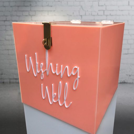 Side angle of 300mm square blush pink acrylic wishing well box with white ‘wishing well’ acrylic script text on front and lock sitting on white plinth.