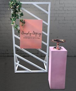 Blush pink plinth and cake stand in front of two separate white window panel backdrops each 2m high by 1m wide. Each frame has 8 diagonal slats.